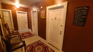 A hallway with numbered doors, a chair, and a sign listing house rules. - Fairview Inn (Talkeetna)
