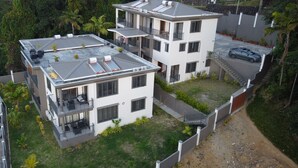 A modern multi-story residential building with a flat roof, balconies, and a small garden area. - Villa Kolibri (Mahé Island)