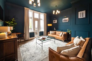 A room with a glass coffee table, leather sofa, and a desk with a lamp.