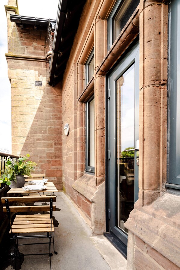A brick building with a glass door entrance, a clock, and outdoor seating with tables and chairs.