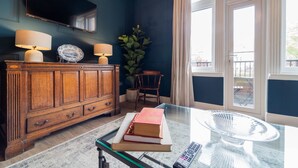 Een kamer met een houten kast, een glazen tafel met boeken, een afstandsbediening en een groot raam met gordijnen.