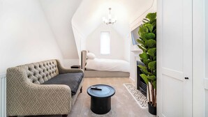 Una habitación acogedora con sofá, una mesita redonda, cama, candelabro y planta en maceta.