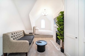 A cozy room with a sofa, a round coffee table, a bed, a chandelier, and a potted plant.