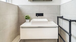 Un baño moderno con un lavabo blanco, una pequeña planta en maceta, un espejo sobre el lavabo y baldosas de suelo con diseño.