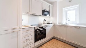 Una cocina moderna con armarios blancos, horno integrado, tetera y ventana.