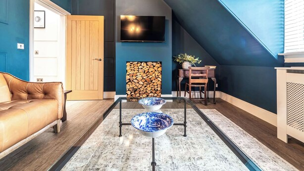 Una sala de estar con un sofá, un televisor montado en la pared, una chimenea con leña a la vista y un comedor con mesa y sillas.