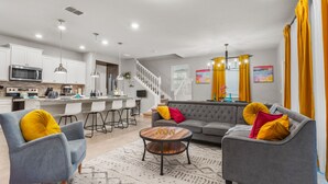 A modern living room with a grey sofa, two armchairs, a coffee table, and a kitchen area in the background.