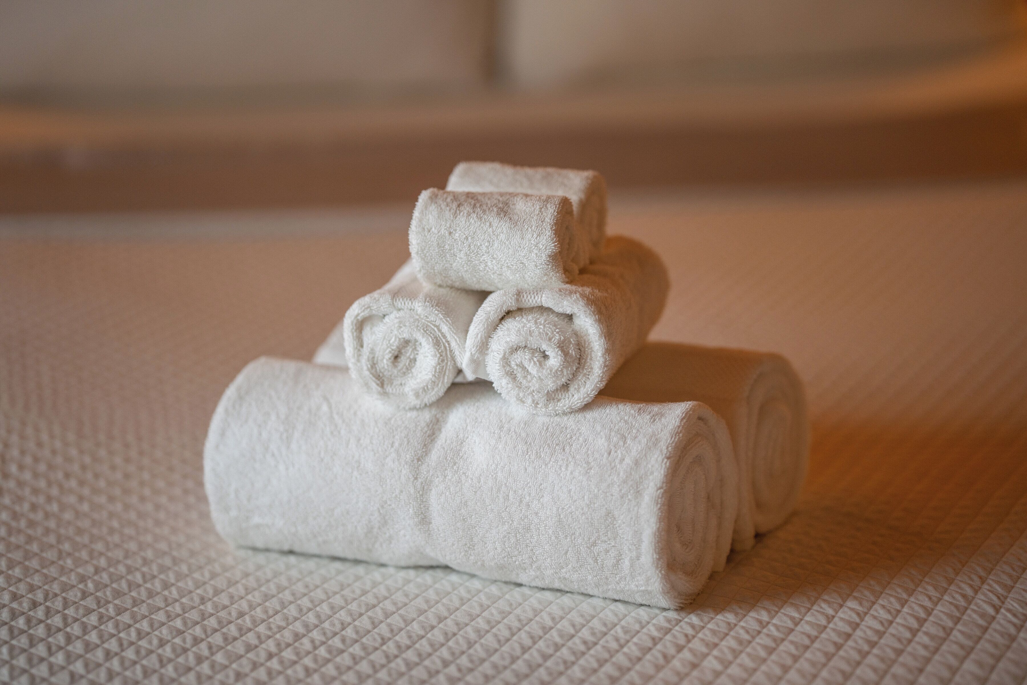 A stack of neatly rolled white towels on a textured white surface.