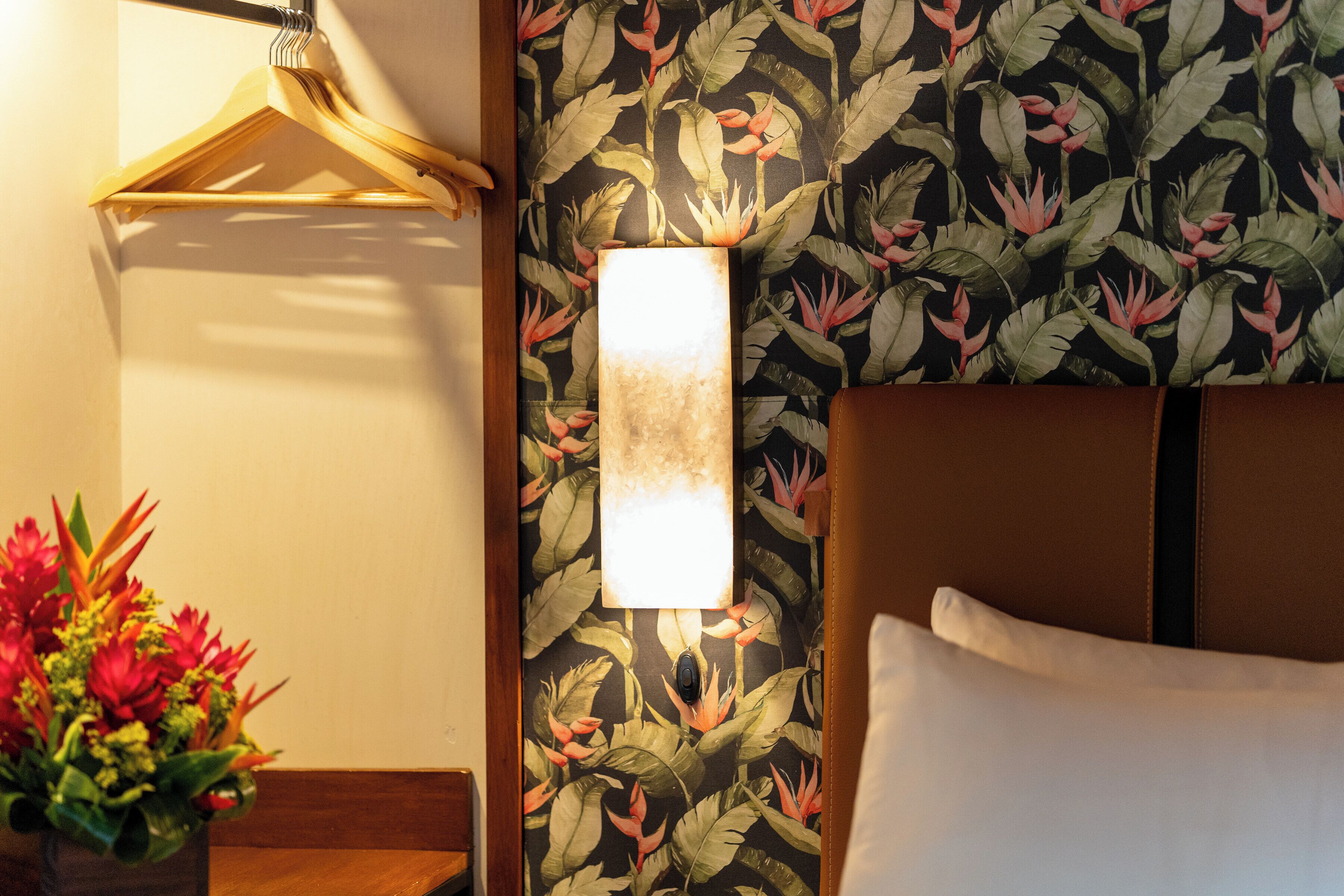 A hotel room with a bed, a wall-mounted light, and a floral wallpaper.