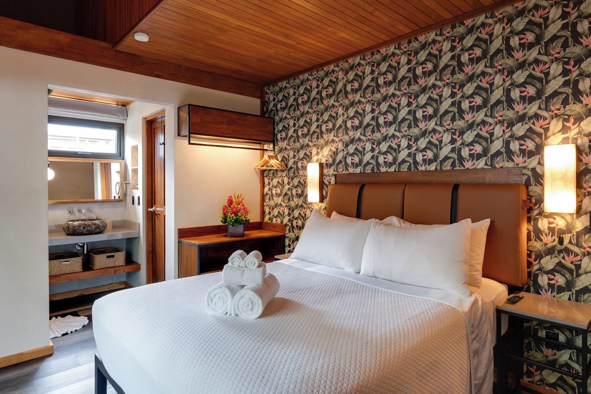 A neatly made bed with rolled towels, a wooden headboard, and a floral wallpaper.