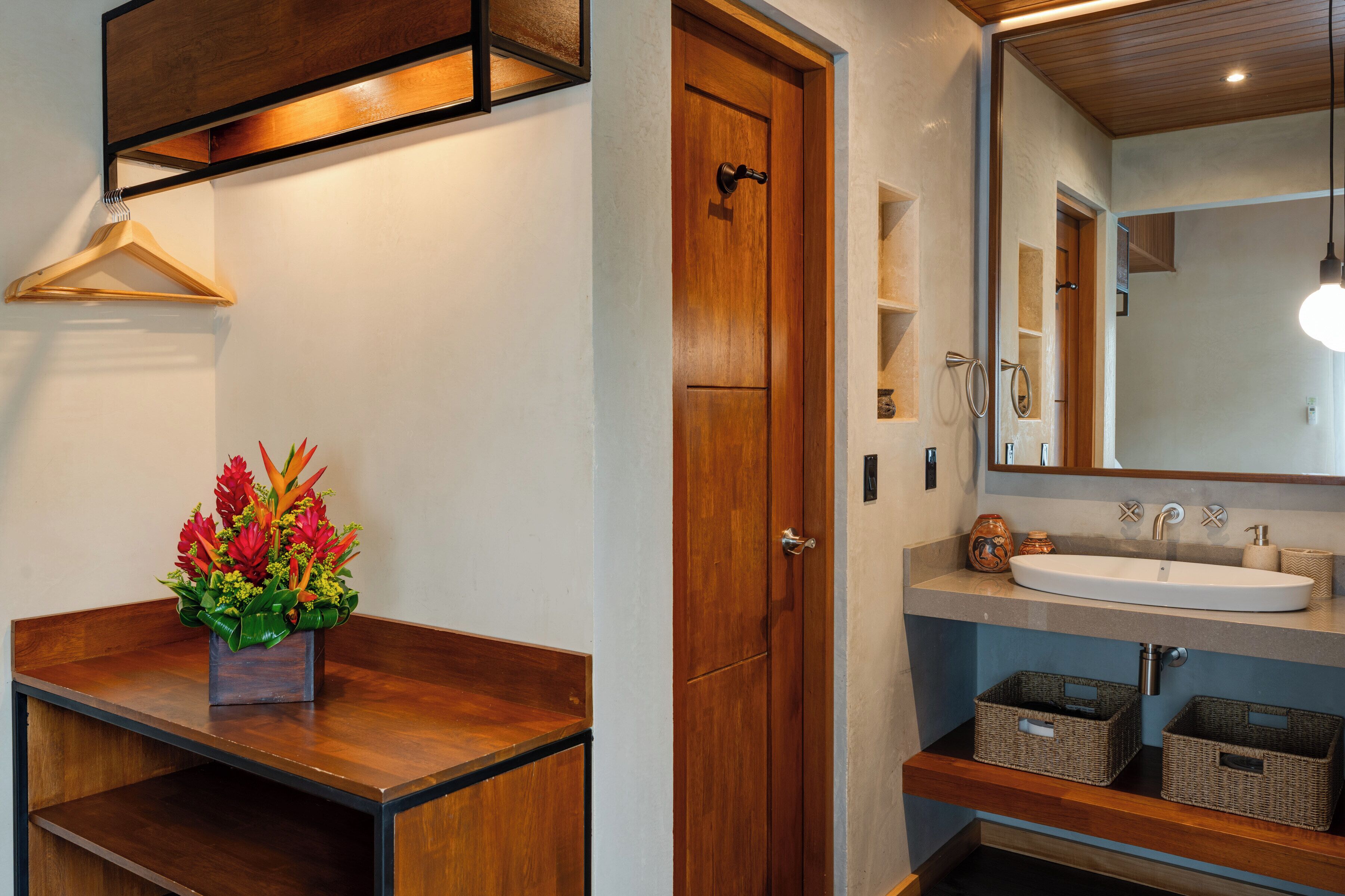 A bathroom with a wooden door, a sink with a mirror, and a wooden shelf with a basket.