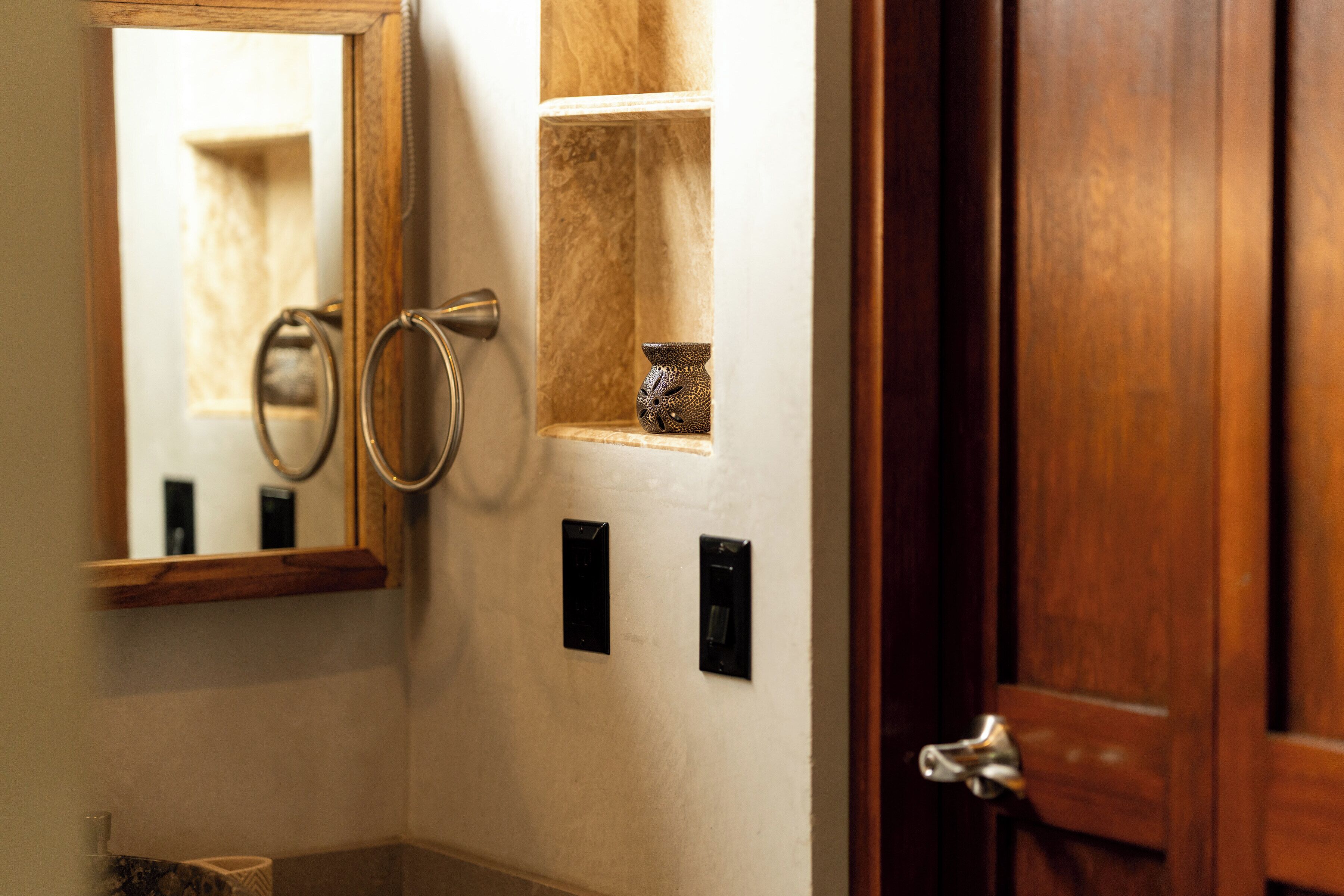 A bathroom with a wooden door, a mirror, a towel ring, and a small shelf with a decorative item.