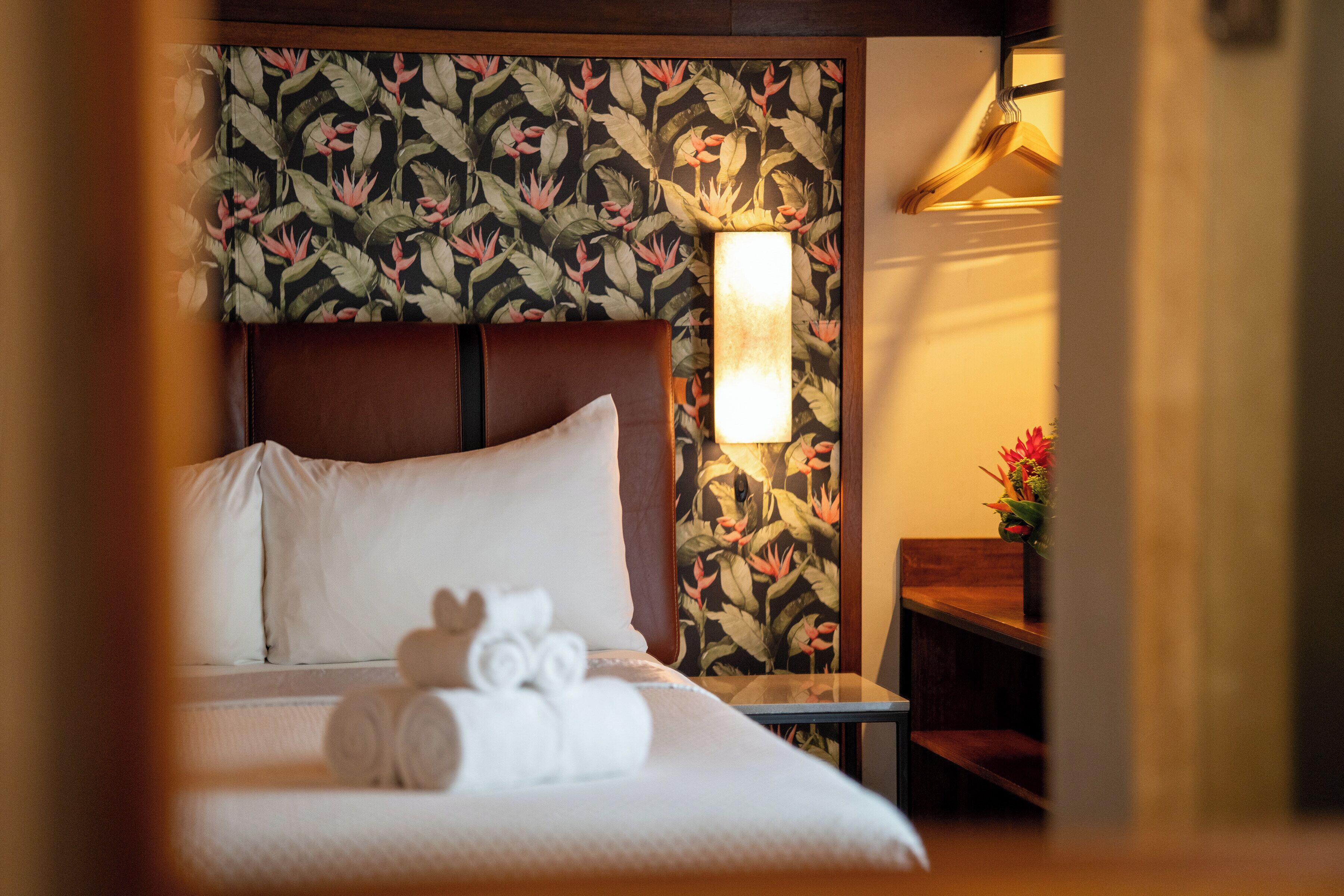 Habitació d'hotel amb llit, almoines, una tauleta de nit, una làmpada i paper tapet floral.