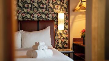 Habitació d'hotel amb llit, almoines, una tauleta de nit, una làmpada i paper tapet floral.