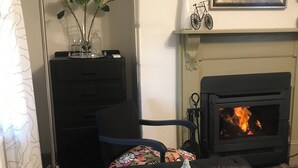 A living room with a fireplace, a black sofa with a pillow, a decorative plant, and a mirror on the wall. - 
Air's Cottage Penola: Colonial stone cottage, WiFi fire AC Spa BBQ dog friendly (Penola)
