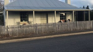 A two-story building with a metal roof and a wooden picket fence. - 
Air's Cottage Penola: Colonial stone cottage, WiFi fire AC Spa BBQ dog friendly (Penola)