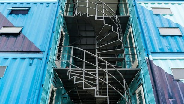 Una escalera de caracol que conduce a un nivel superior de un edificio con paredes exteriores azules.