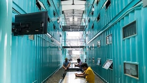 Un pasillo estrecho con paredes color turquesa y una mesa central donde hay personas sentadas.