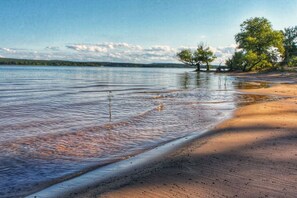 A beach with clear water, a sandy shore, and trees in the background. - The Perfect Porch Retreat! (Eufaula)