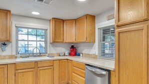 A kitchen with wooden cabinets, a stainless steel refrigerator, and a window with blinds.