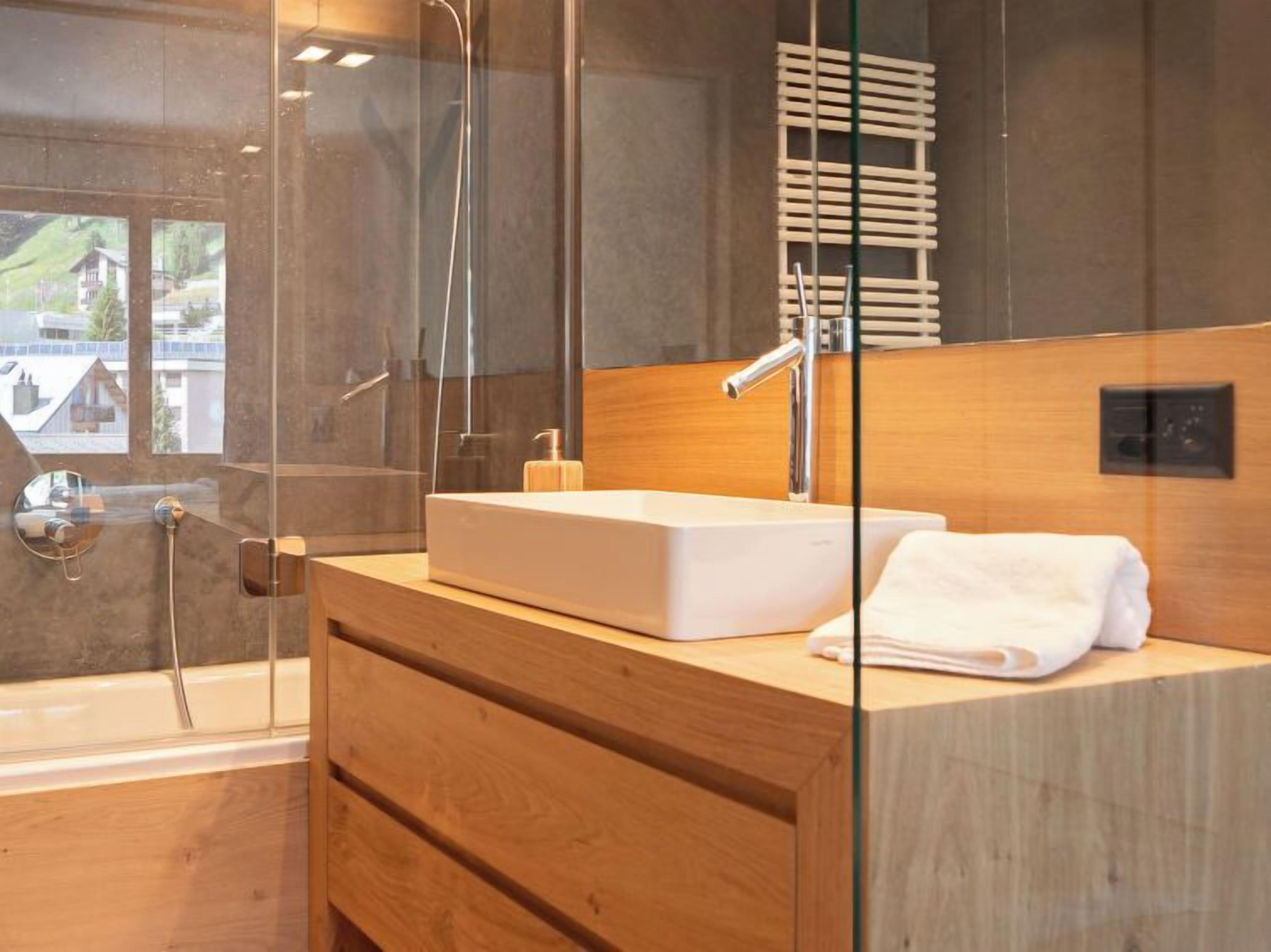 Een moderne badkamer met een douchecabine van glas, een houten wastafelmeubel met een wastafel, en een handdoek op het aanrecht.