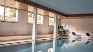 Piscina interna com paredes de vidro transparente, vigas de madeira e um mural na parede.
