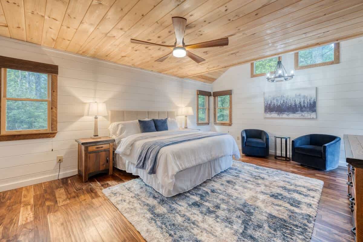A bedroom with a bed, bedside tables, a ceiling fan, a chandelier, and a painting on the wall.