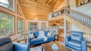 A spacious living area with a wooden ceiling, a sofa, a coffee table, and a staircase leading to an upper level. - Pineview Escape - Hot tub, arcade & mountain views (Blue Ridge Mountains)