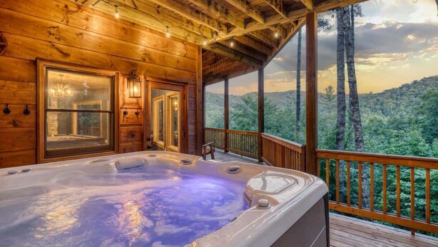 A wooden cabin with a hot tub, large windows, and a deck overlooking a forested area. - Pineview Escape - Hot tub, arcade & mountain views (Blue Ridge Mountains)
