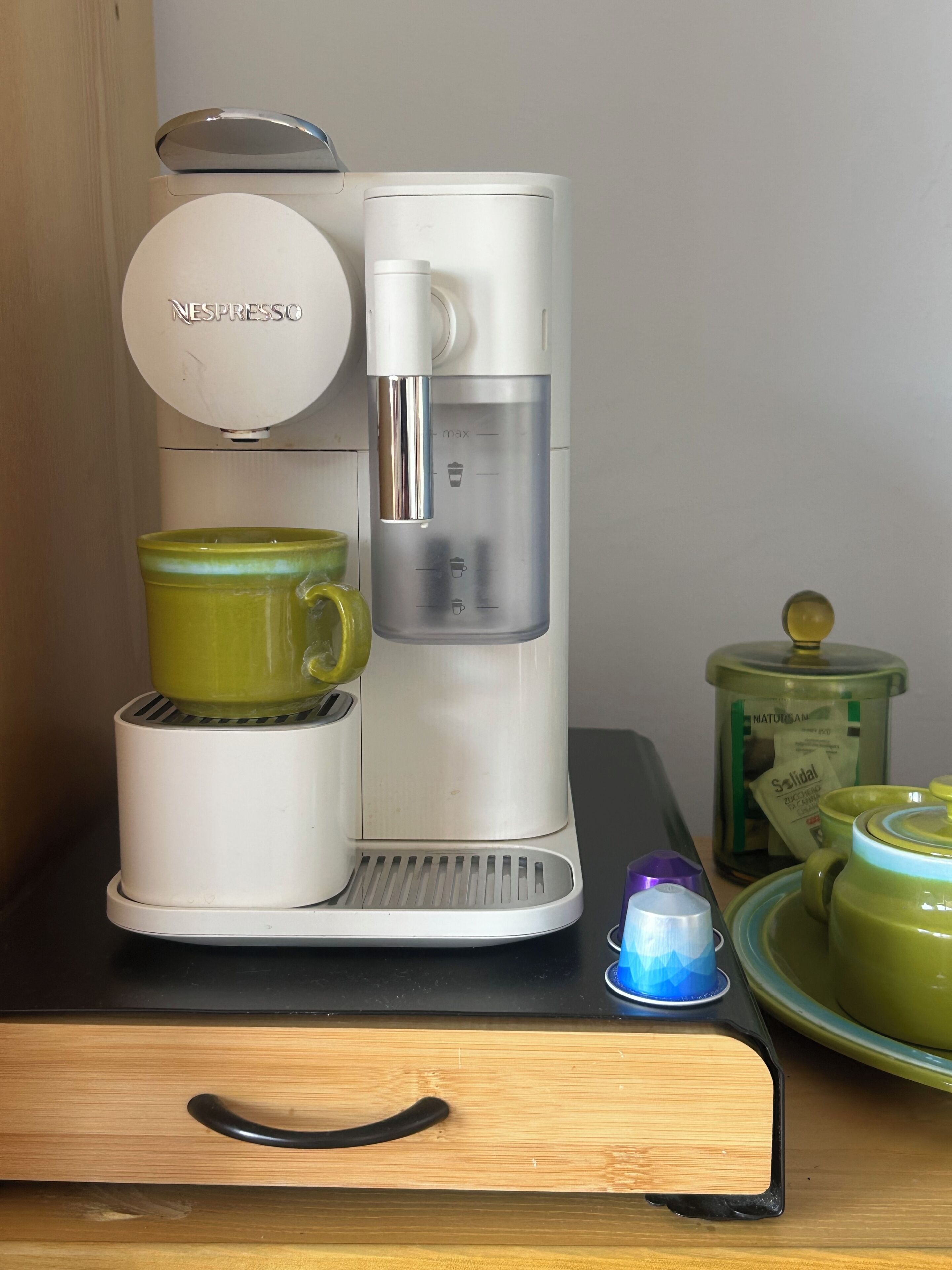 Une machine à café Nespresso avec une tasse verte, un petit récipient bleu et un récipient vert doté d’un couvercle.
