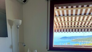 A hotel room with a bed, a window with a view, a bedside table, and a lamp. - Sea view Terrace, Pool, Direct Sea Access in Residence with Tennis (Rosignano Marittimo)