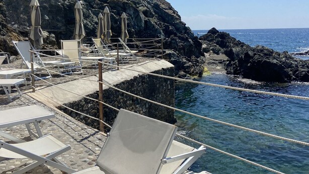 A rocky beach with white lounge chairs and umbrellas. - Sea view Terrace, Pool, Direct Sea Access in Residence with Tennis (Rosignano Marittimo)