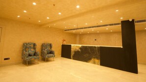 A reception area with two patterned chairs, a reception desk, and a marble wall. - Dolphin club and Resort (Lucknow)