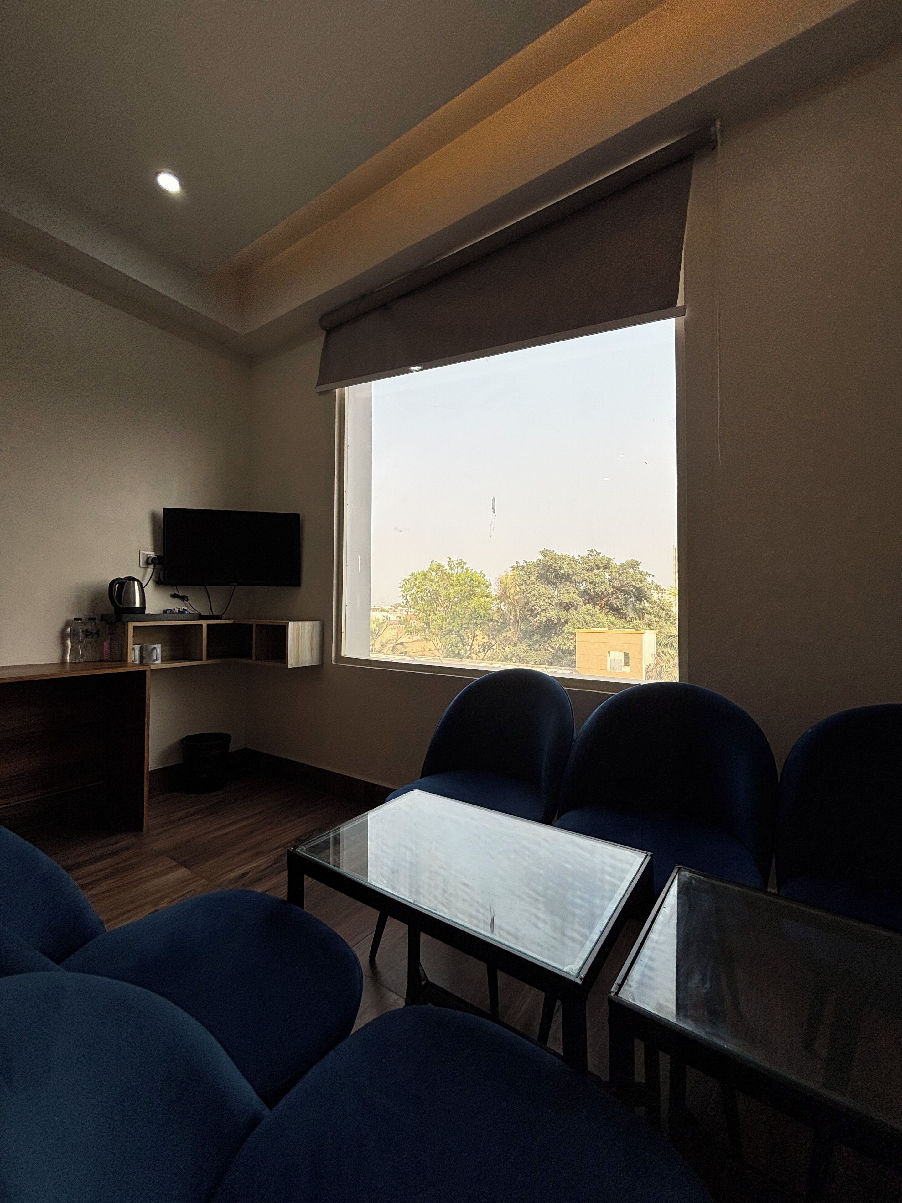 Habitación de hotel con una ventana grande, un televisor de pantalla plana, una mesita pequeña y varias sillas.