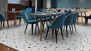 A modern dining area with a terrazzo floor, blue upholstered chairs, and a ceiling with recessed lighting and hanging pendant lights. - Dolphin club and Resort (Lucknow)