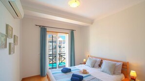 Ein Hotelzimmer mit Bett, Nachttisch mit Lampe, Fenster mit Vorhängen und Blick nach draußen.