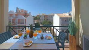 Ein Balkon mit einem Tisch, gedeckt für ein Frühstück, mit Orangensaft, Ananas und Gebäck.