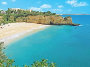 A coastal beach with a sandy shore, a cliff, and buildings in the background. - Sunny Beach Retreat by Interhome (Armação de Pêra)