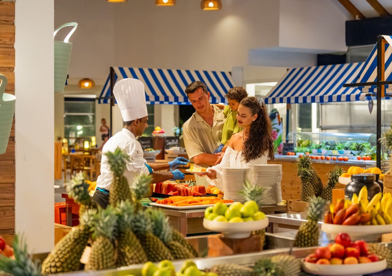 Zona de buffet con diversas frutas y un chef preparando comida.
