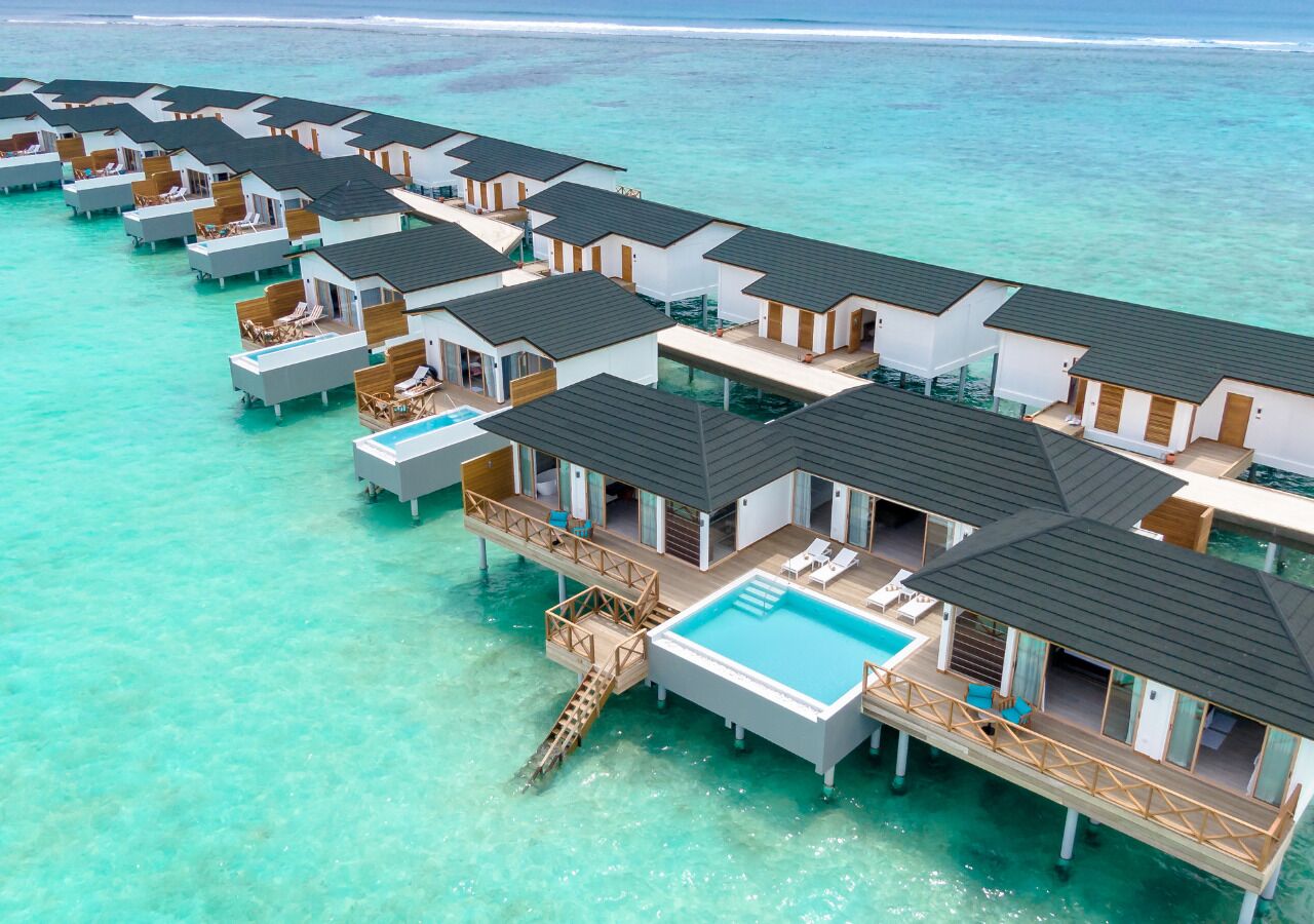 Cabañas sobre el agua con piscinas privadas, conectadas por senderos, ubicadas en aguas turquesas cristalinas.