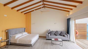 A modern bedroom with a bed, a gray sofa, a small table, and a ceiling fan.