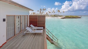 A wooden deck with two white lounge chairs and a small table, overlooking a clear turquoise sea and a sandy beach with palm trees. - Joy Island  (Kasanfaru Island)