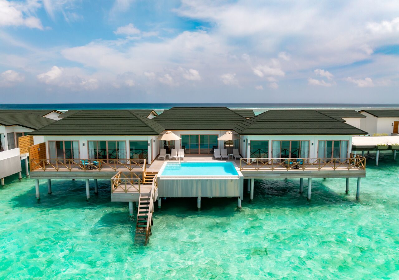 A resort with overwater bungalows connected by walkways, featuring a central pool and ocean views.