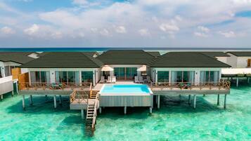 A resort with overwater bungalows connected by walkways, featuring a central pool and ocean views.