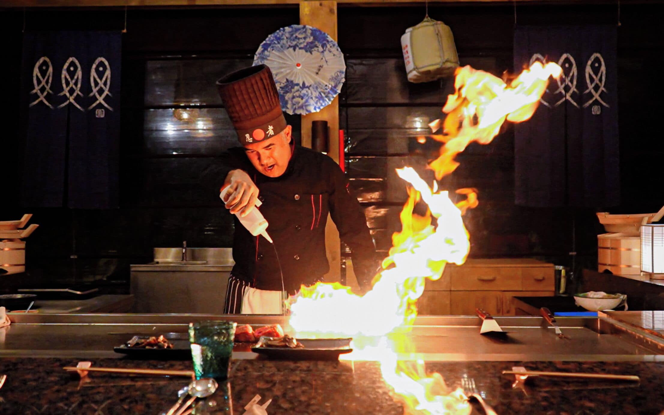 Un chef realiza una flambé con una botella de licor en una cocina.
