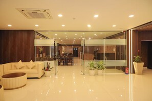 Een moderne hotel lobby met een zithoek, een receptiebalie en een eetgedeelte.