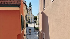 A narrow street with buildings on either side, a church with a green dome in the distance, and a cyclist in the middle of the street. - Győr (Gyor)