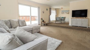 A living room with a sofa, a dining table with chairs, a television on a cabinet, and a star decoration on the wall. - The Look Out (Norwich)