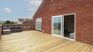 A wooden deck with a brick wall, a sliding glass door, and outdoor seating. - The Look Out (Norwich)