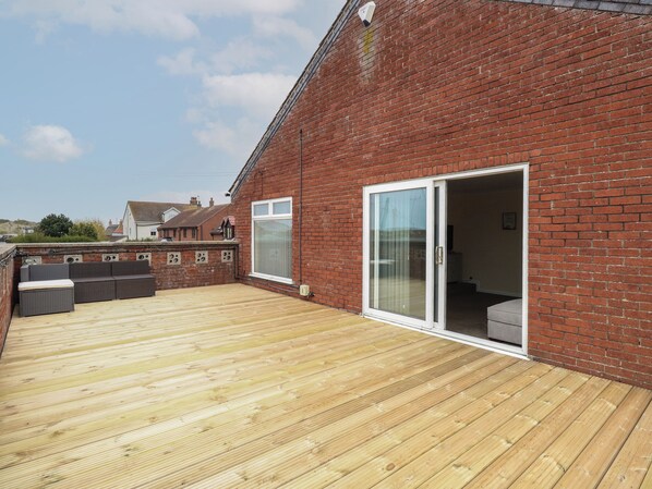 A wooden deck with a brick wall, a sliding glass door, and outdoor seating.